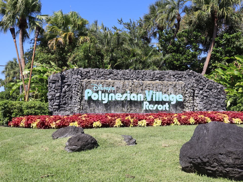 entrance sign to polynesian resort with palm trees and flowers