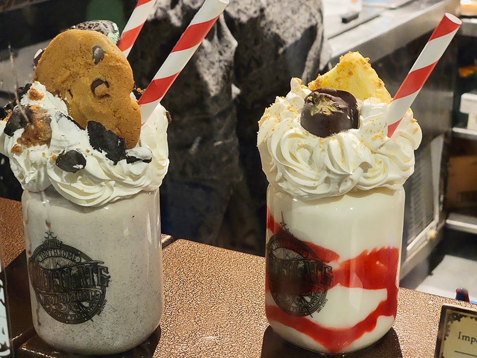 two tall milkshakes with full toppings over a jar