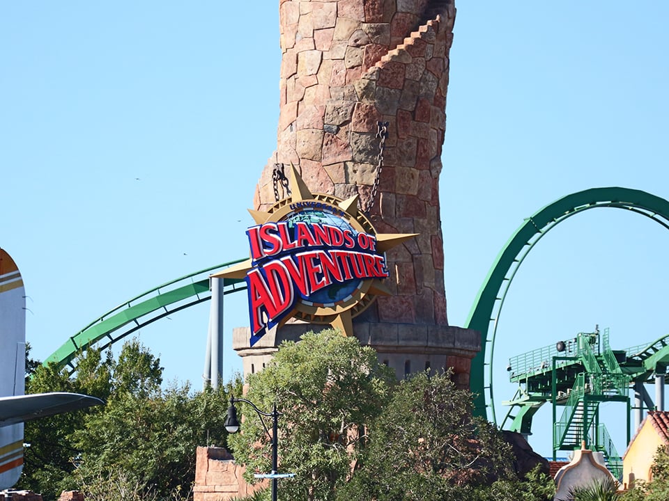 entrance sign for islands of adventure in orlando with coaster in background