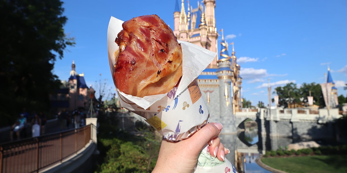 a woman holds a turkey leg in front of cinderella's castle